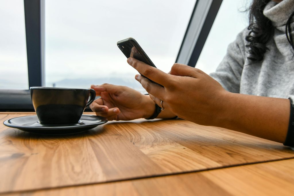 A woman enjoys coffee while browsing her smartphone in a modern café setting.