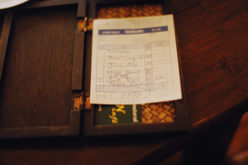 Close-up of a restaurant bill placed on a dark wooden table, creating a moody ambiance.